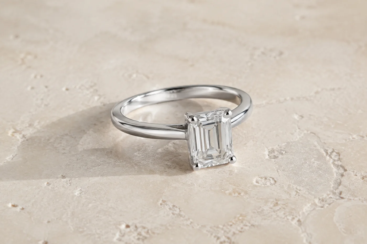 Illustrative platinum solitaire ring with an emerald-cut diamond on pale stone
